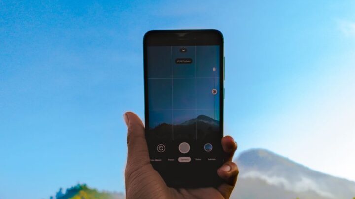 Dłoń trzyma smartfon podczas fotografowania górskiego krajobrazu.