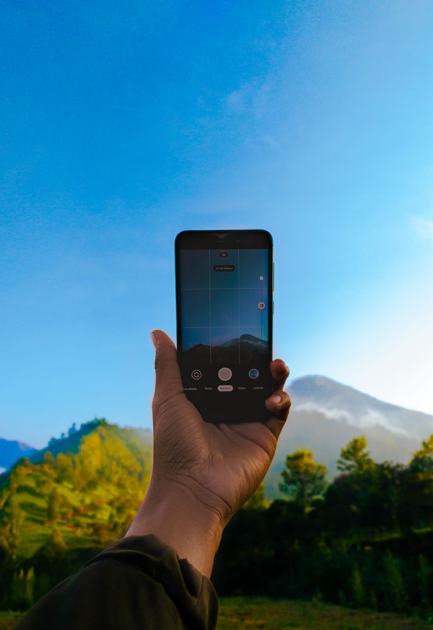 Dłoń trzyma smartfon podczas fotografowania górskiego krajobrazu.