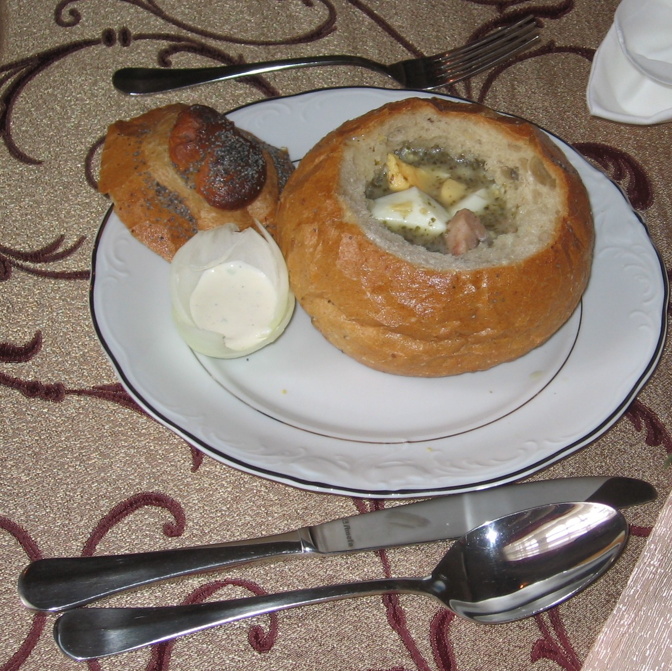 Żurek podany w wydrążonym pieczywie z dodatkami na talerzu