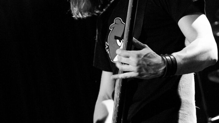 Mariusz Duda gra na gitarze basowej podczas koncertu Riverside. Fotografia czarno-biała.