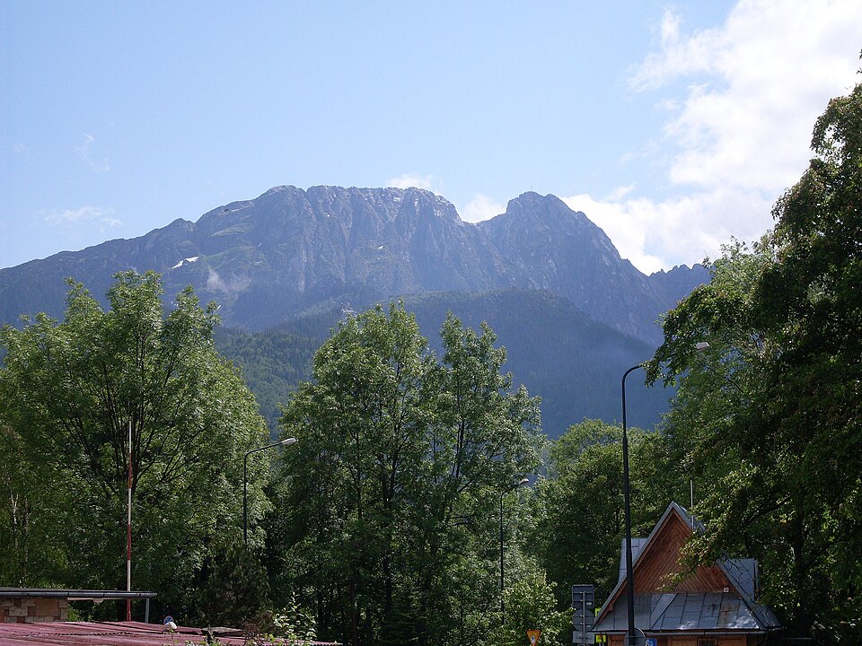 Archiwalny widok na Giewont z Zakopanego, z drzewami i zabudową na pierwszym planie.