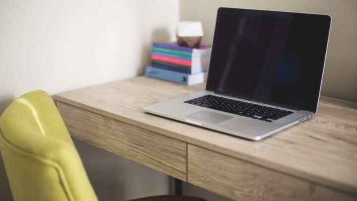 Laptop z ciemnym ekranem na biurku obok stosu książek
