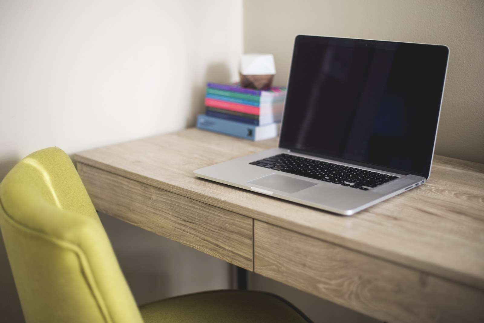 Laptop z ciemnym ekranem na biurku obok stosu książek