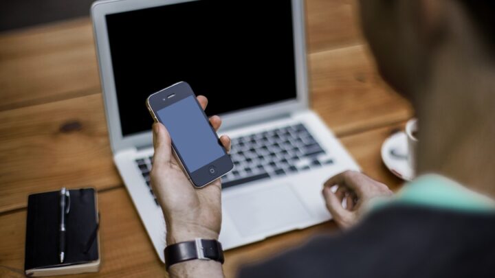 Telefon trzymany obok otwartego laptopa