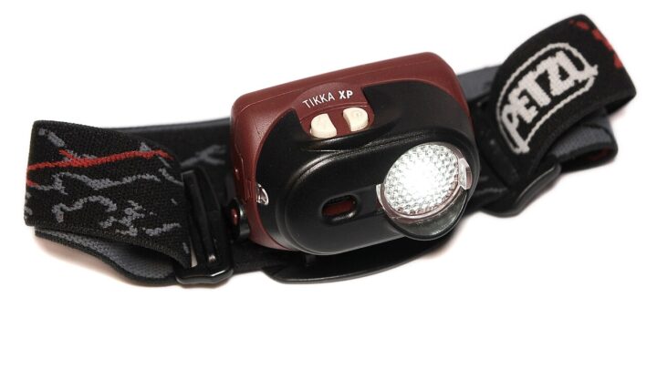 Archiwalna fotografia czołówki Petzl Tikka XP z paskiem na białym tle.