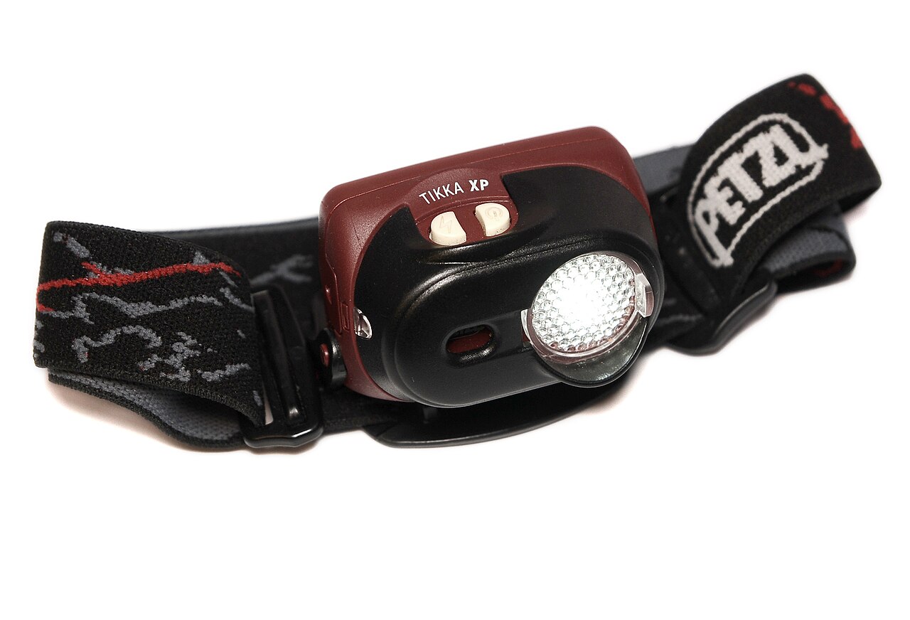 Archiwalna fotografia czołówki Petzl Tikka XP z paskiem na białym tle.