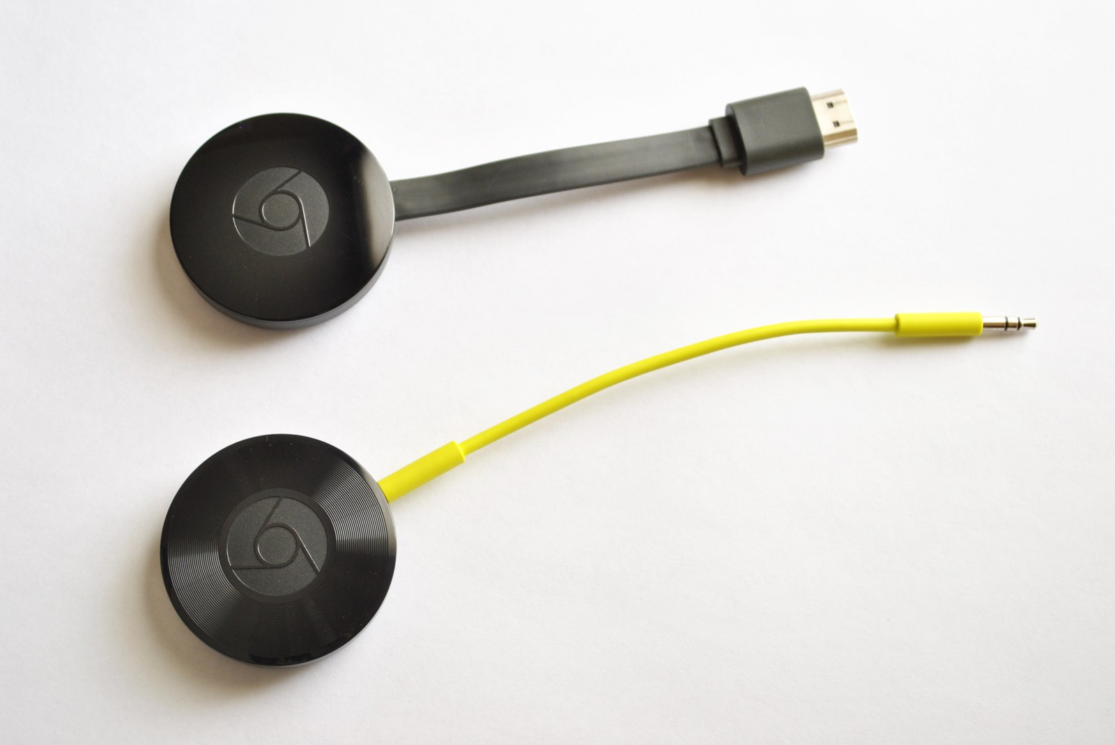 Chromecast drugiej generacji z przewodem HDMI u góry oraz Chromecast Audio z żółtym przewodem u dołu.